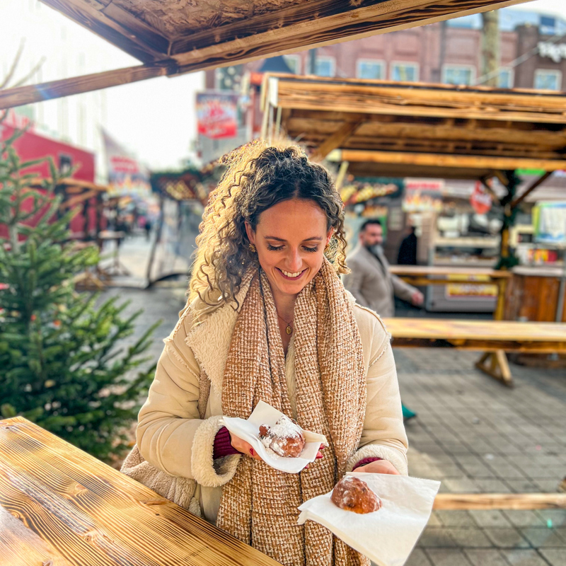 Vrouw kijkt met een glimlach naar een oliebol in haar hand. 