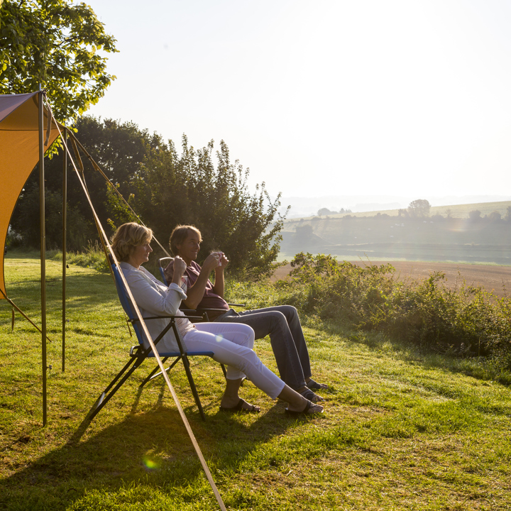 Echtpaar in campingstoel voor de tent met een kopje koffie, genieten van het uitzicht. 