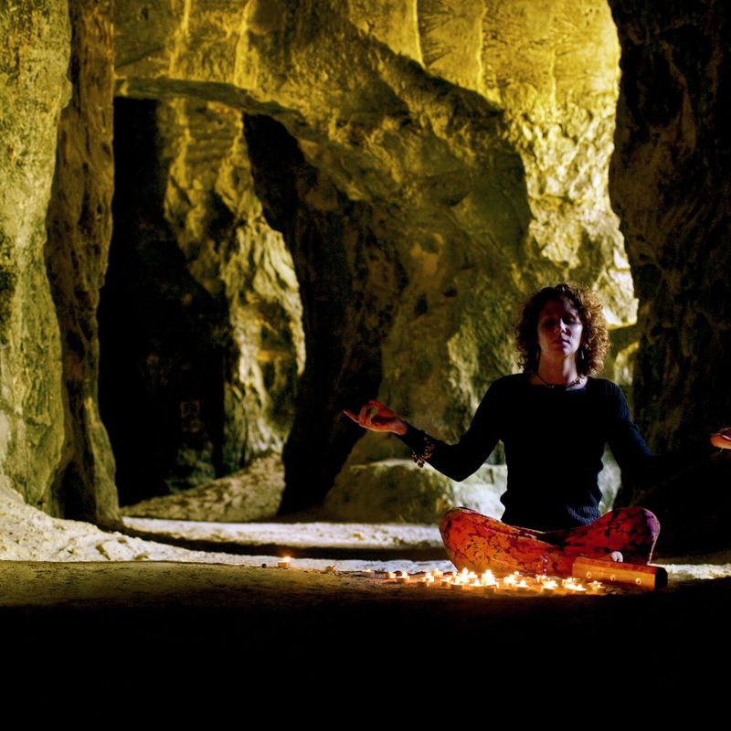 Mediterende vrouw in grot met brandende kaarsjes op de voorgrond