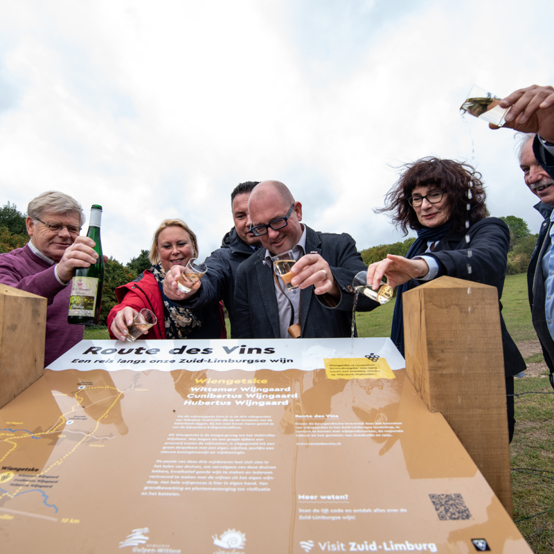 De onthulling van de Route des Vins Wahlwiller-Eys, waarbij verschillende personen het wijnbord inwijden door het te dopen met een glaasje wijn