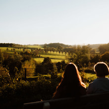 twee mensen zitten op een bankje met ondergaande zon en bekijken het heuvelachtige Landschap 