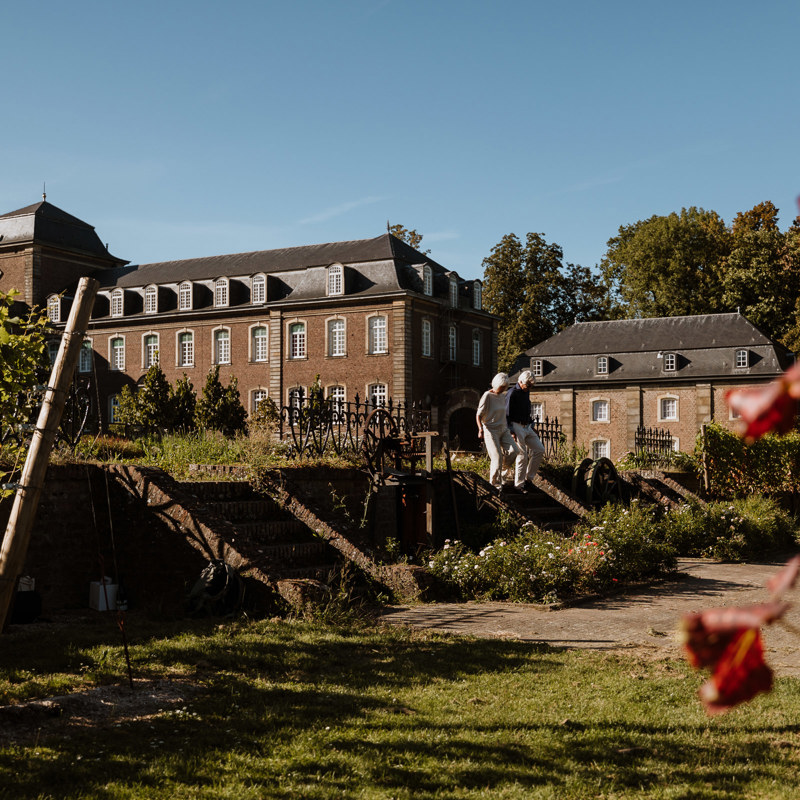 Een man en vrouw dalen een trapje af naar de wijngaard van Abdij Rolduc