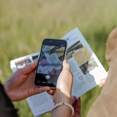 Bezoekers scannen met telefoon een QR-code in een drukwerk tijdens de wandeling. 