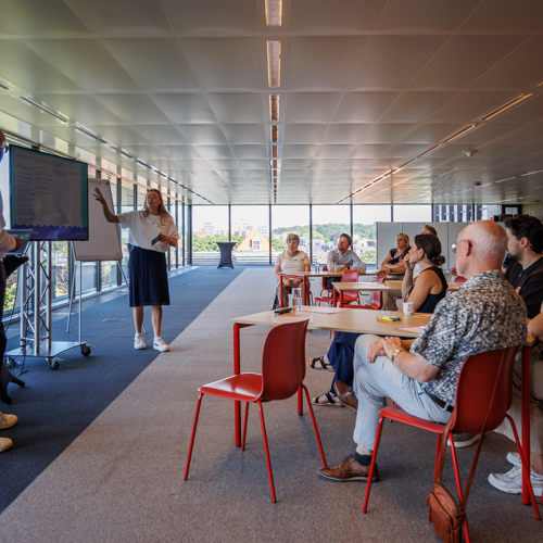 Twee personen geven presentatie aan een zaal met mensen. 