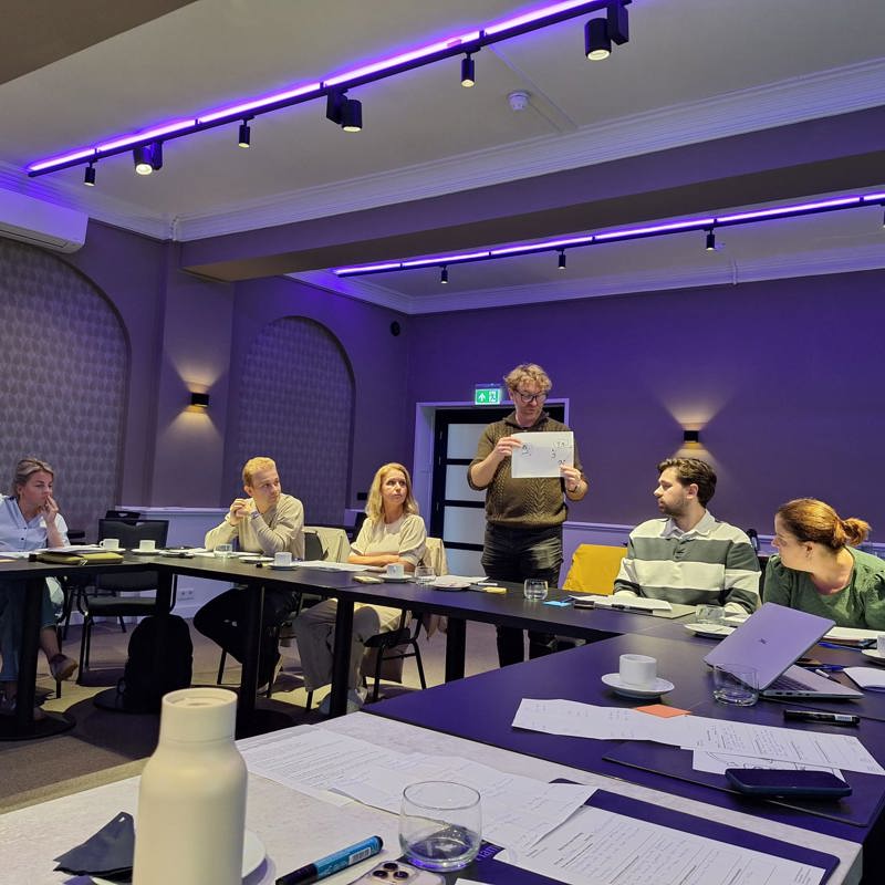 Ondernemers aan tafel waarbij één ondernemer zijn idee presenteert aan de rest van de groep.